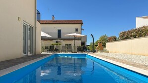 Ein Schwimmbecken mit Liegestühlen, ein Gebäude mit Ziegeldach und ein klarer Himmel.