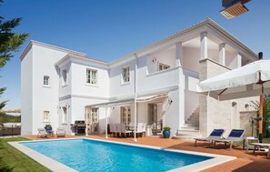 Ein großes, weißes, zweistöckiges Haus mit Swimmingpool, Außenmöbeln und einer überdachten Terrasse.