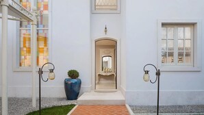 Entrada de um edifício com piso de azulejos, um vaso azul grande e duas luminárias fixadas na parede.