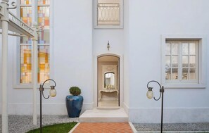 Ein Gebäudeeingang mit Fliesenboden, einem großen blauen Blumentopf und zwei Wandleuchten.