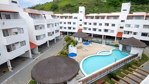 A hotel with multiple white buildings, a swimming pool, and a thatched-roof structure. - Seu Lar na Praia Grande (Arraial do Cabo)