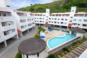 Un hotel con varias edificaciones blancas, una piscina y una estructura con techo de paja.