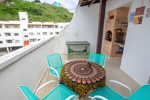 A balcony with a table and chairs, a small table, and a brick wall. - Seu Lar na Praia Grande (Arraial do Cabo)