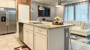 A modern kitchen with a central island, white cabinetry, a built-in dishwasher, and a large window. - 5BR Home with Pool and Game Room Disney (Davenport)