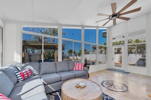Ein geräumiges Wohnzimmer mit grauem Sofa, einem Holztisch und einem Deckenventilator.