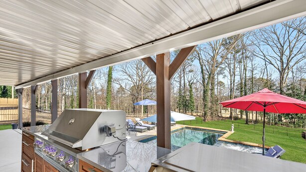 Eine Außenküche mit Grill, integriertem Stauraum und Blick auf Pool und Garten.