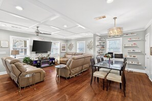 A modern living room with a leather recliner, a glass dining table, and a flat-screen TV mounted on the wall. - World Cup Luxury • Pool/Hot Tub •Walkable • On Golf Course • Prime  Atl location (Atlanta)