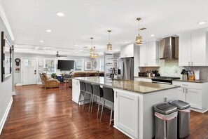 A modern kitchen with white cabinetry, a central island with bar stools, stainless steel appliances, and pendant lighting. - World Cup Luxury • Pool/Hot Tub •Walkable • On Golf Course • Prime  Atl location (Atlanta)