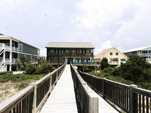 Eine Holzboden-Promenade führt zu einem mehrstöckigen Gebäude mit Balkonen und Blick auf den Strand.