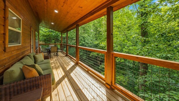 Une terrasse en bois avec un canapé et un panier en osier, donnant sur une forêt.