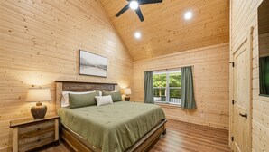 Une chambre aux murs lambrissés, avec un lit, des lampes de chevet, un ventilateur de plafond et une fenêtre avec des rideaux.