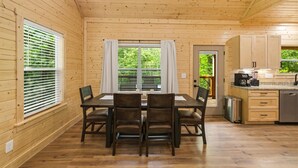 Une cabane en bois comprenant un coin repas, une cuisine et offrant une vue sur la verdure environnante.