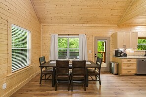 A wooden cabin with a dining area, kitchen, and a view of greenery outside. - Modern, Cozy Cabin Close to Major Attractions! (Pigeon Forge)