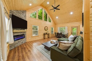 A cozy cabin interior with a fireplace, wooden walls, a dining area, and a ceiling fan. - Modern, Cozy Cabin Close to Major Attractions! (Pigeon Forge)