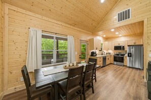 A wooden cabin interior with a dining area, kitchen, and a window with blinds. - Modern, Cozy Cabin Close to Major Attractions! (Pigeon Forge)