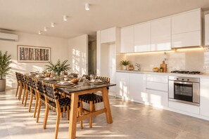 A modern kitchen with white cabinetry, a dining table set for six, and a built-in oven. - Signature Lake View Luxury Residences H19 (San Carlos de Bariloche)