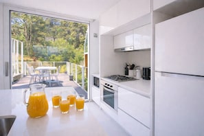 Eine moderne Küche mit einem großen Fenster, einem Essbereich mit Außenbestuhlung und einem Glas mit Orangensaft.