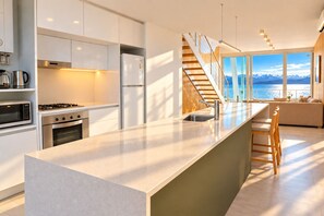 A modern kitchen with a large island, stainless steel appliances, and a view of the mountains through large windows. - Signature Lake View Luxury Residences H19 (San Carlos de Bariloche)