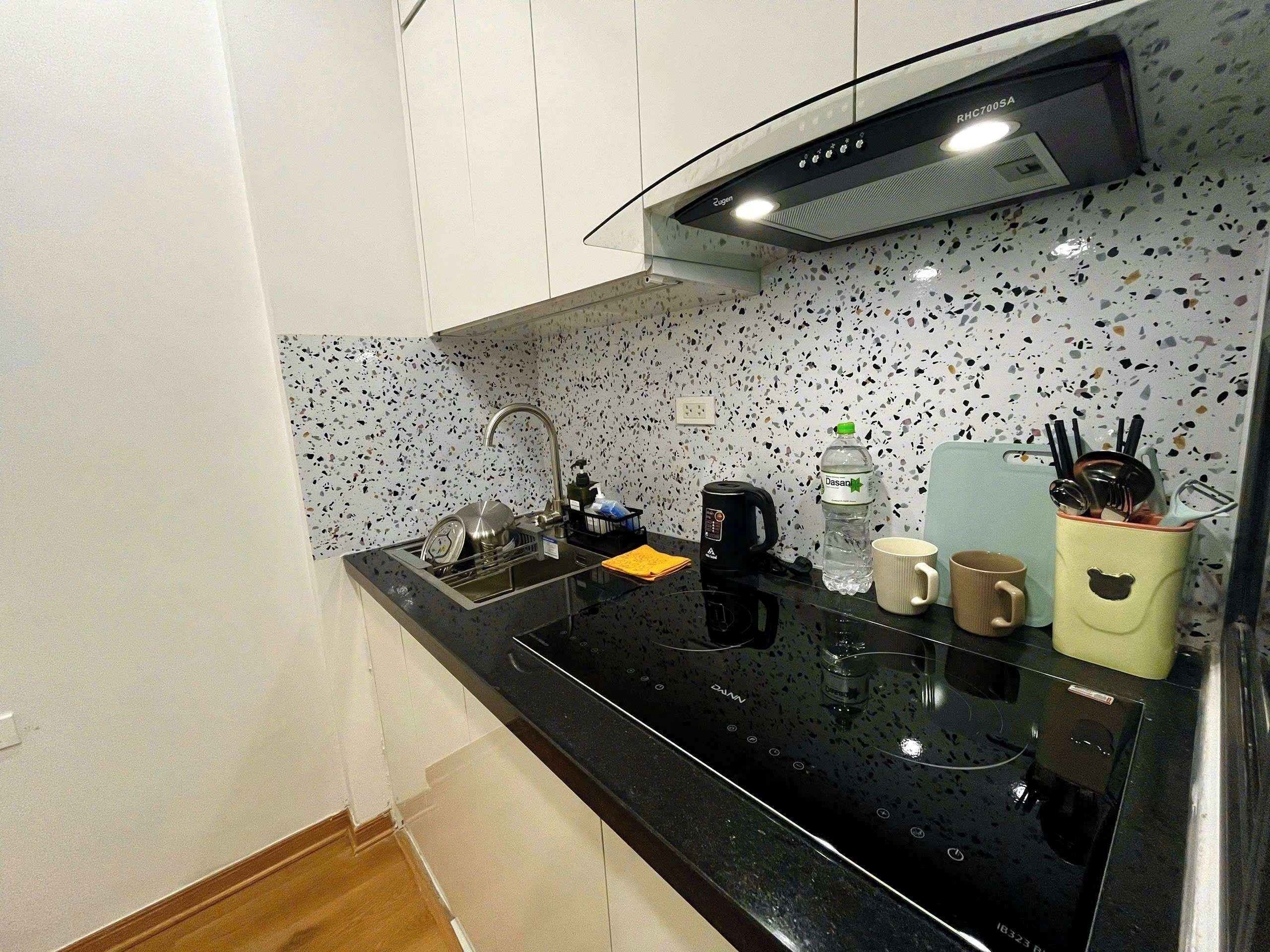 A kitchen with a black countertop, a coffee maker, a water bottle, a mug, and a bear-shaped container.