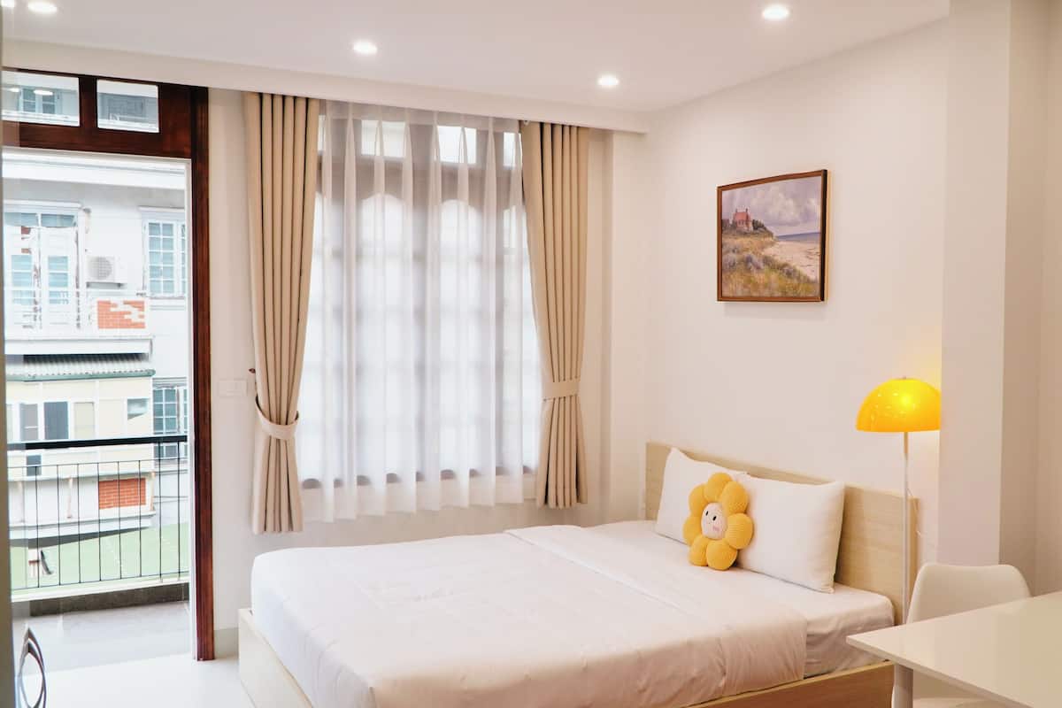 Une chambre d’hôtel avec un lit, un bureau, une lampe, une fenêtre avec des rideaux et un tableau au mur.