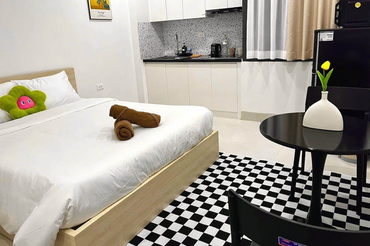 Une chambre d’hôtel avec un lit, une petite table, une chaise, un coin cuisine et un sol à carreaux.