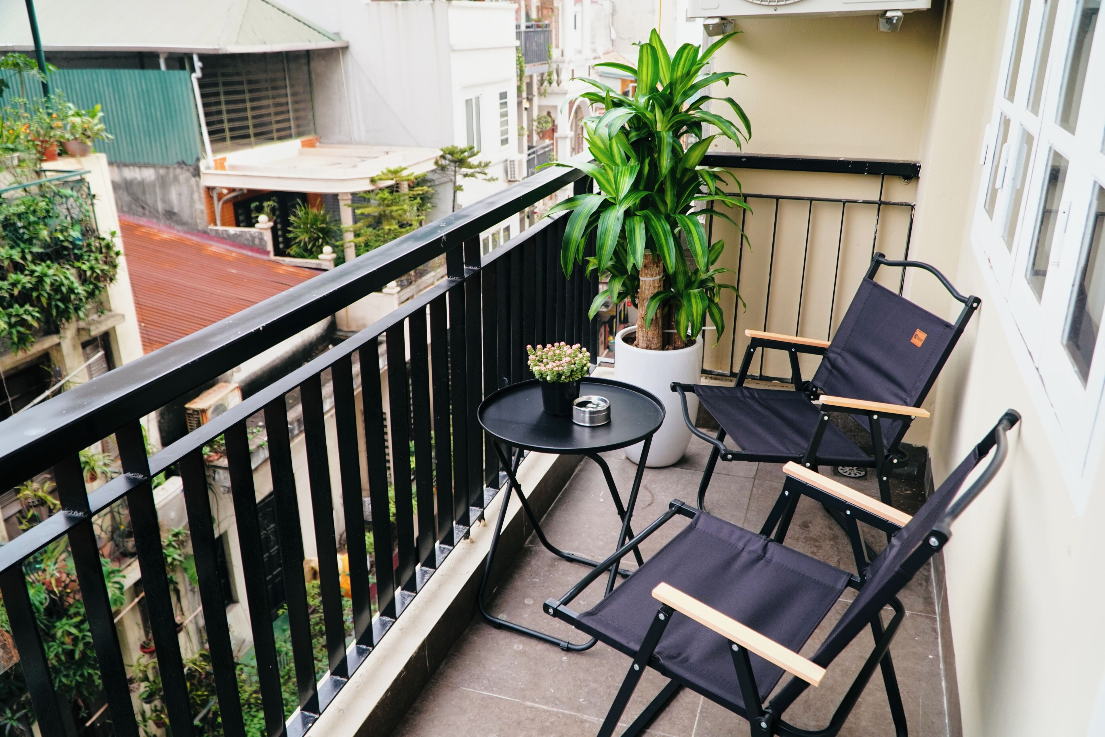 A balcony with a black railing, two black folding chairs, a small round table, and a potted plant.