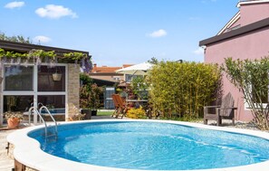 A swimming pool with a stone border, a wooden deck, and a garden area with plants and a chair.