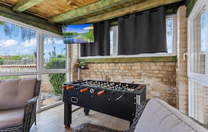 A cozy room with a foosball table, a comfortable sofa, and a television mounted on a stone wall.