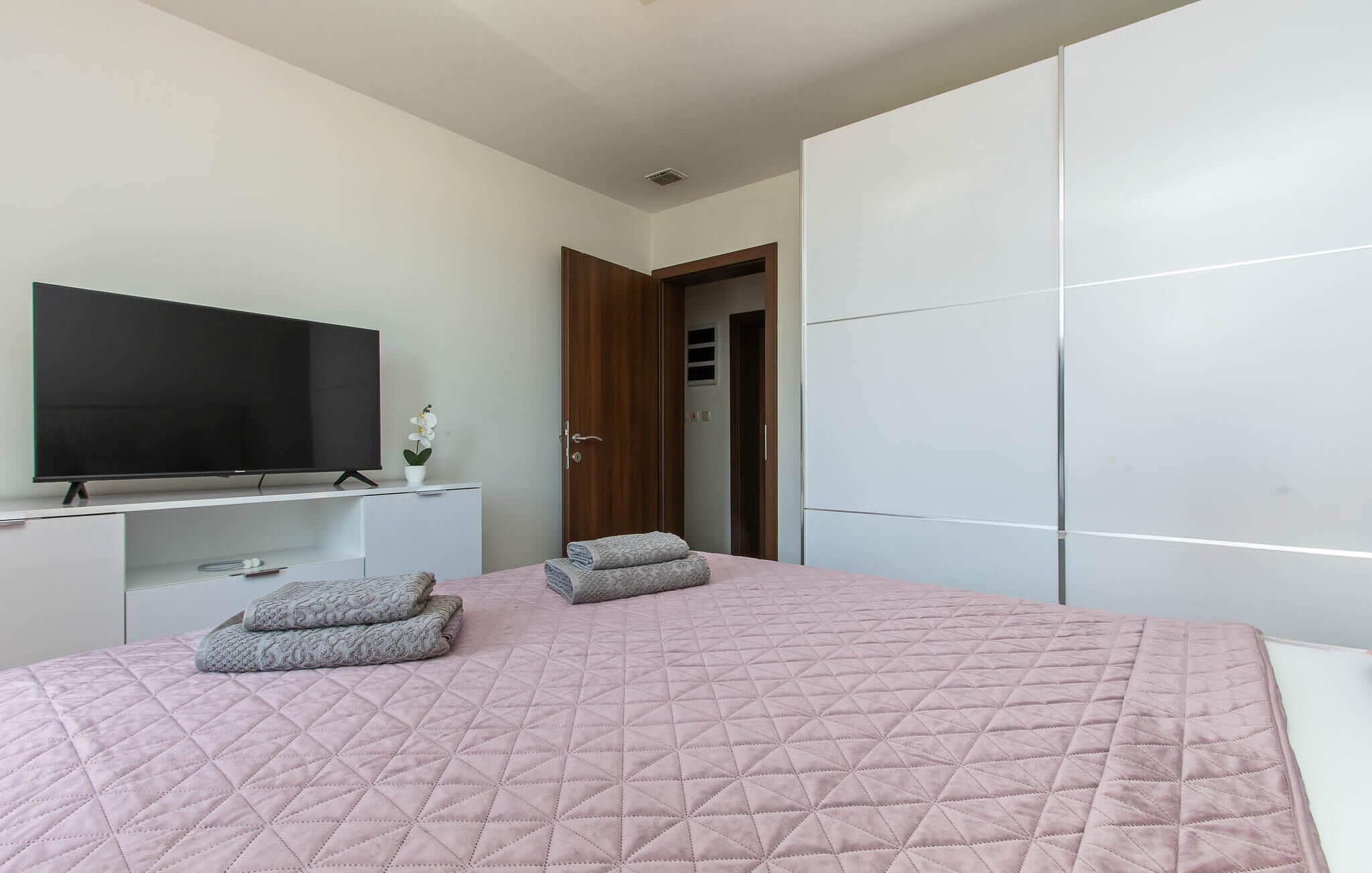Une chambre à coucher comprenant un lit, une télévision, une armoire et une porte donnant sur une autre pièce.