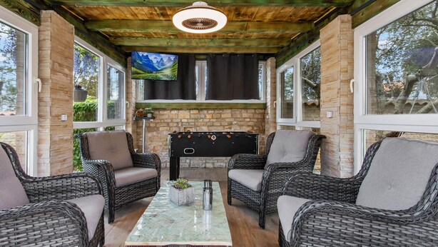Un espacio de estar al aire libre cubierto con mobiliario de mimbre, una chimenea y una pantalla de televisión.