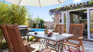 Un patio al aire libre con piscina, sillas de madera, una mesa y una parrilla.