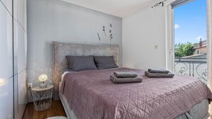 Un dormitorio con cama, almohadas, una lámpara de noche y vistas al exterior.