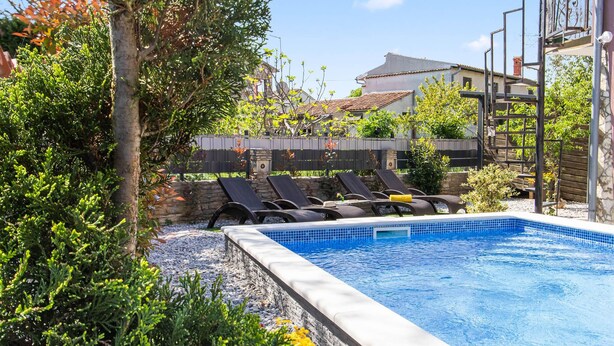 A swimming pool with lounge chairs, surrounded by greenery and a stone wall. - Awesome home in Jursici (Jursici)