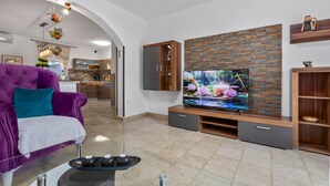 A modern living room with a large flat-screen TV, a purple sofa, and a kitchen in the background. - Awesome home in Jursici (Jursici)