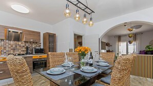A modern kitchen with a dining area, featuring a round table with chairs, a vase with flowers, and a hanging light fixture. - Awesome home in Jursici (Jursici)