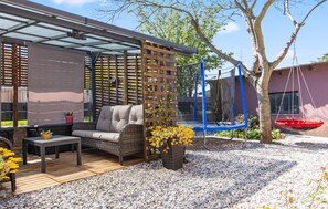 Eine Terrasse mit einer Couch, einem Tisch, einem Holzzimmer und einem Trampolin.