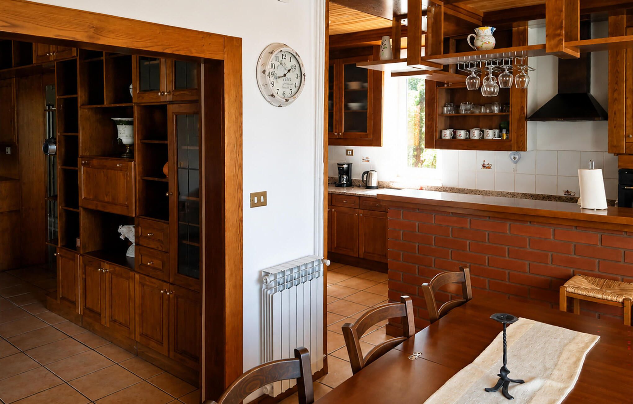 A kitchen with wooden cabinets, a brick wall, a dining table with chairs, and a hanging light fixture.