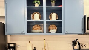 Een keuken met blauwe kastjes, een roestvrijstalen spoelbak, een koffiezetapparaat en een magnetron.