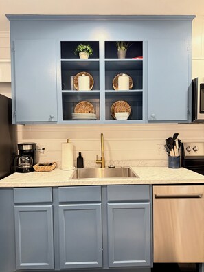Una cocina con armarios azules, un lavamanos de acero inoxidable, una cafetera y un microondas.