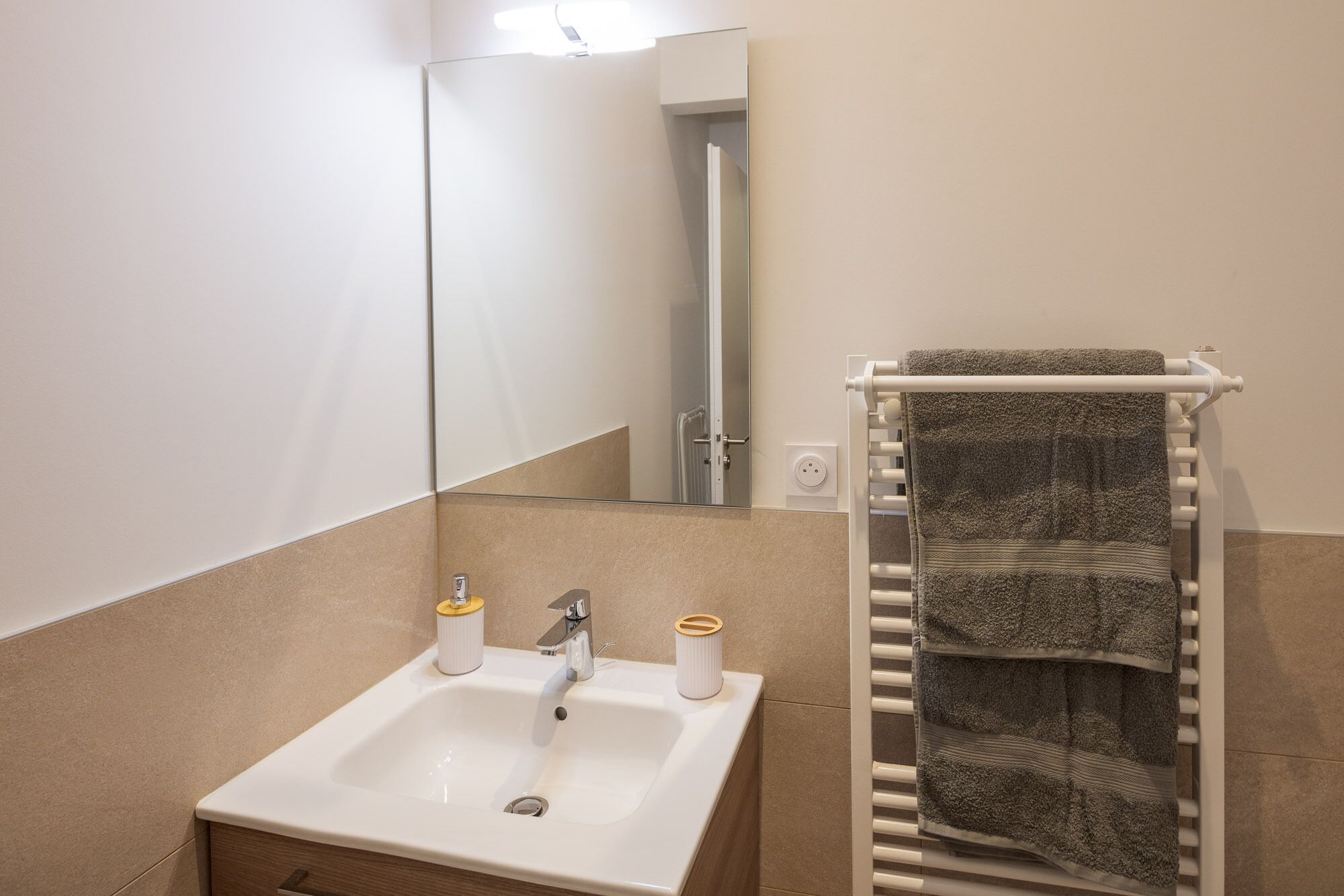 Un baño con lavamanos blanco, espejo, toallero y una puerta que da a la ducha.