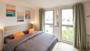 Ein Schlafzimmer mit einem Bett, zwei Bildern, einem Fenster und Vorhängen.