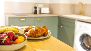 Eine Küche mit Waschmaschine, einem Teller mit Croissants und einer Schüssel Obst.