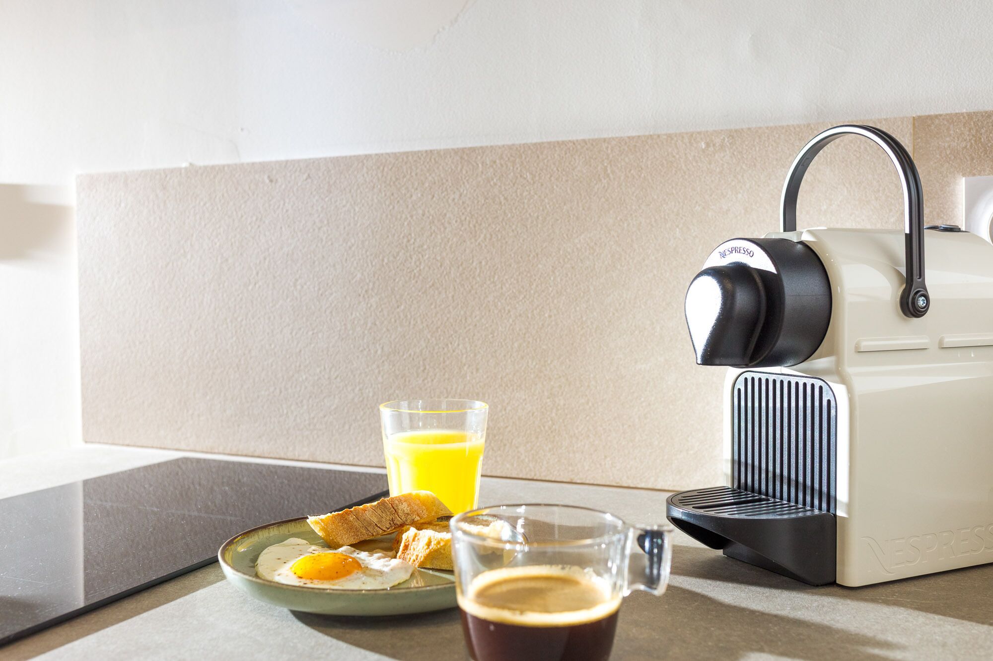 A kitchen with a coffee machine, a plate with eggs, toast, and a glass of orange juice.