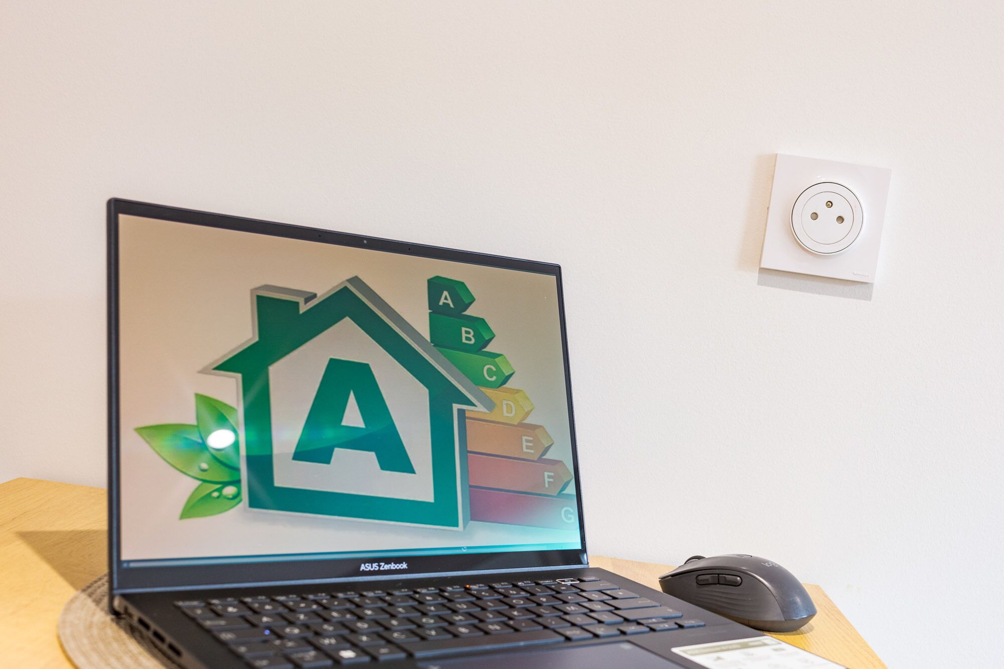 A laptop on a desk with a keyboard, a mouse, and a wall socket.