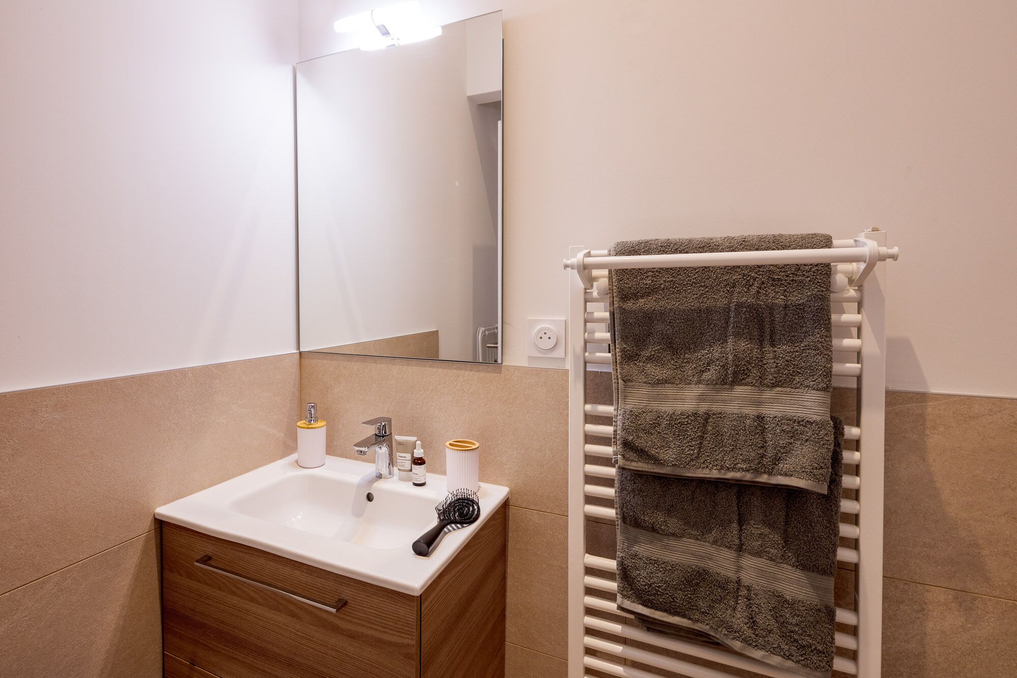 A bathroom with a sink, mirror, towel rack, and toiletries.
