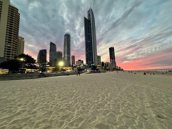 Ein Strand mit Sand und einer Stadtlandschaft im Hintergrund.