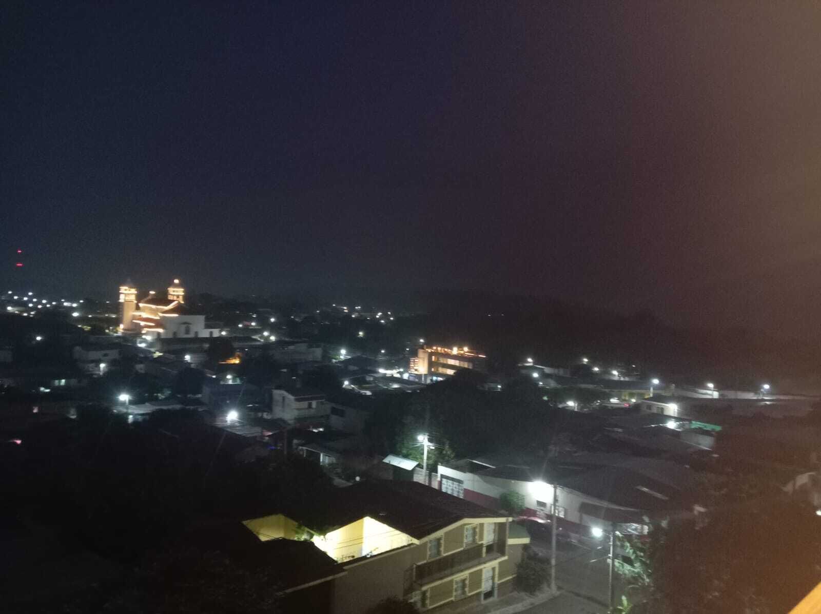 Une vue nocturne d’une ville, avec ses bâtiments illuminés et une tour imposante qui se distingue.