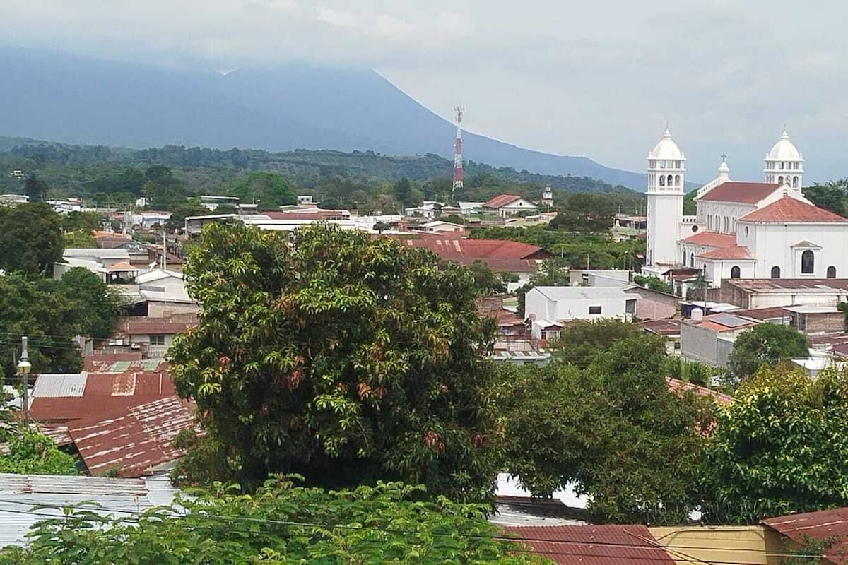 Une ville qui se distingue par une église blanche imposante, des bâtiments aux toits rouges et une montagne en arrière-plan.