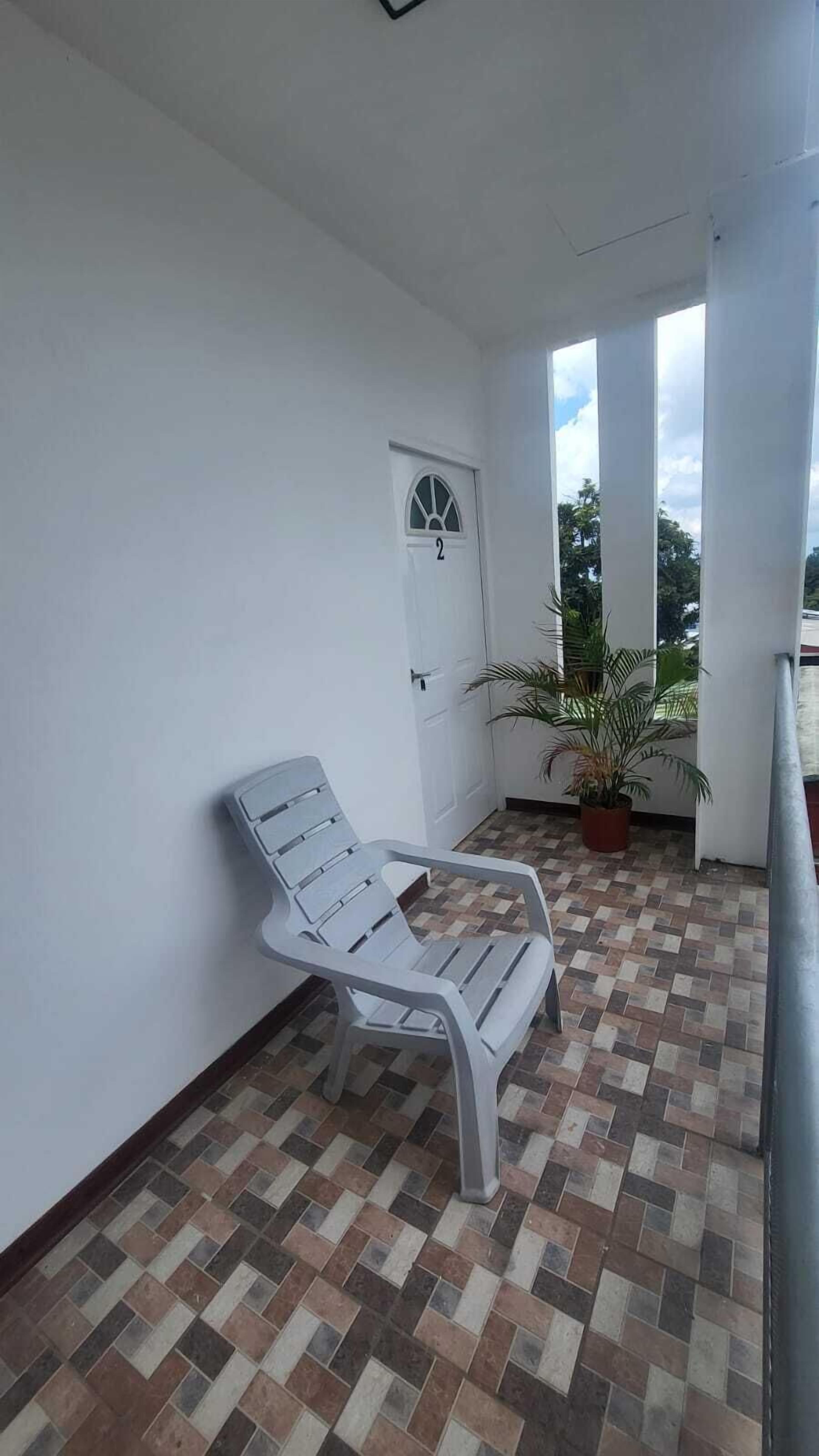 Een balkon met een witte stoel, een bloempot en een deur met het nummer 2.