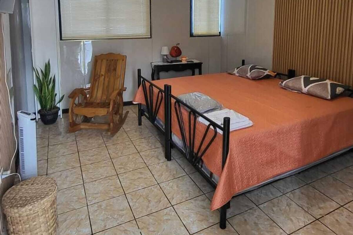 Une chambre à coucher avec un lit, une chaise, une télévision et une fenêtre.